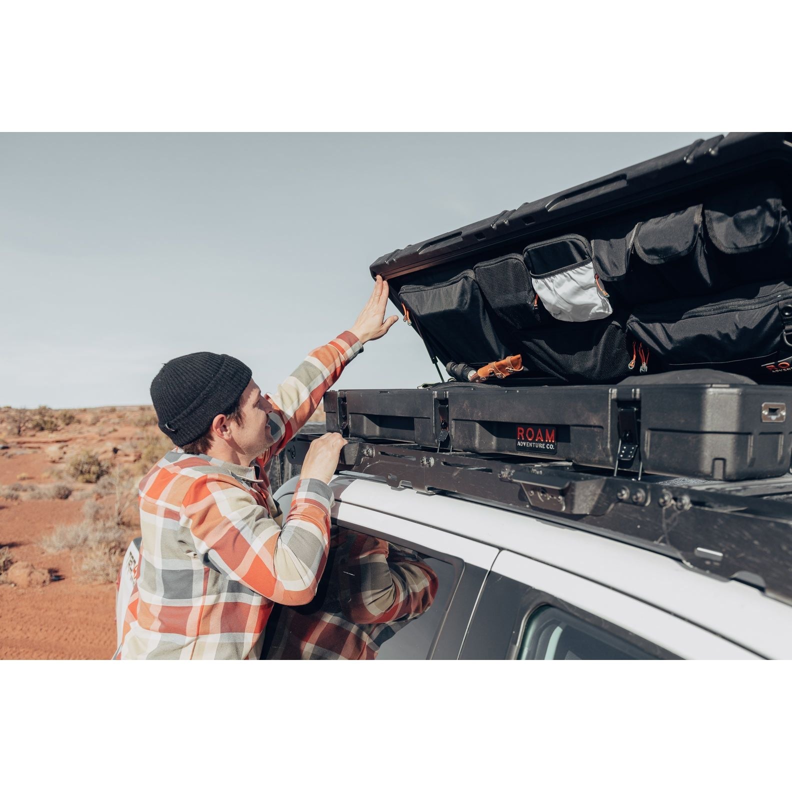 Man using the lid organizer of a low-profile 83L Rugged Case mounted on top of a vehicle